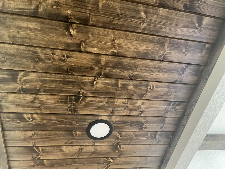 Close-up of a knotty stained tongue-and-groove wood ceiling with a recessed light