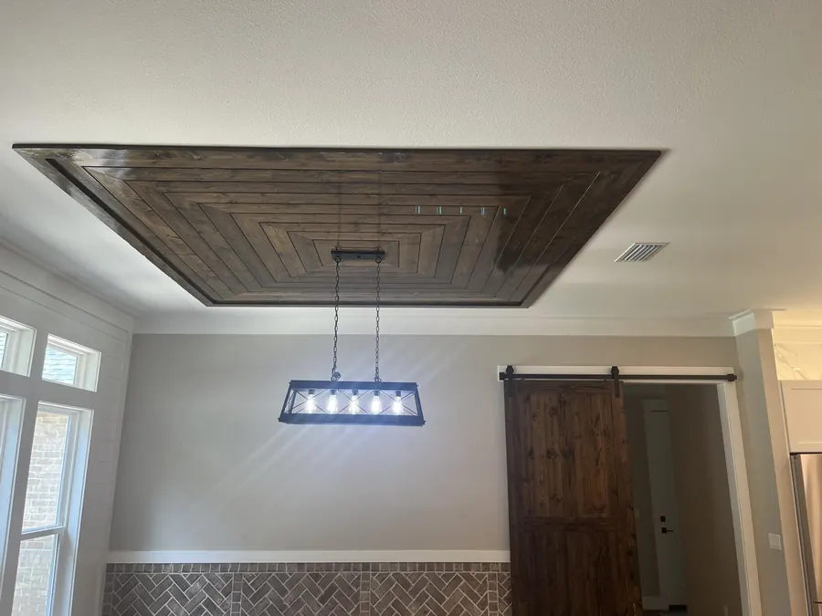 Dining room with a stained wood tray ceiling and a rectangular iron chandelier beside a barn door