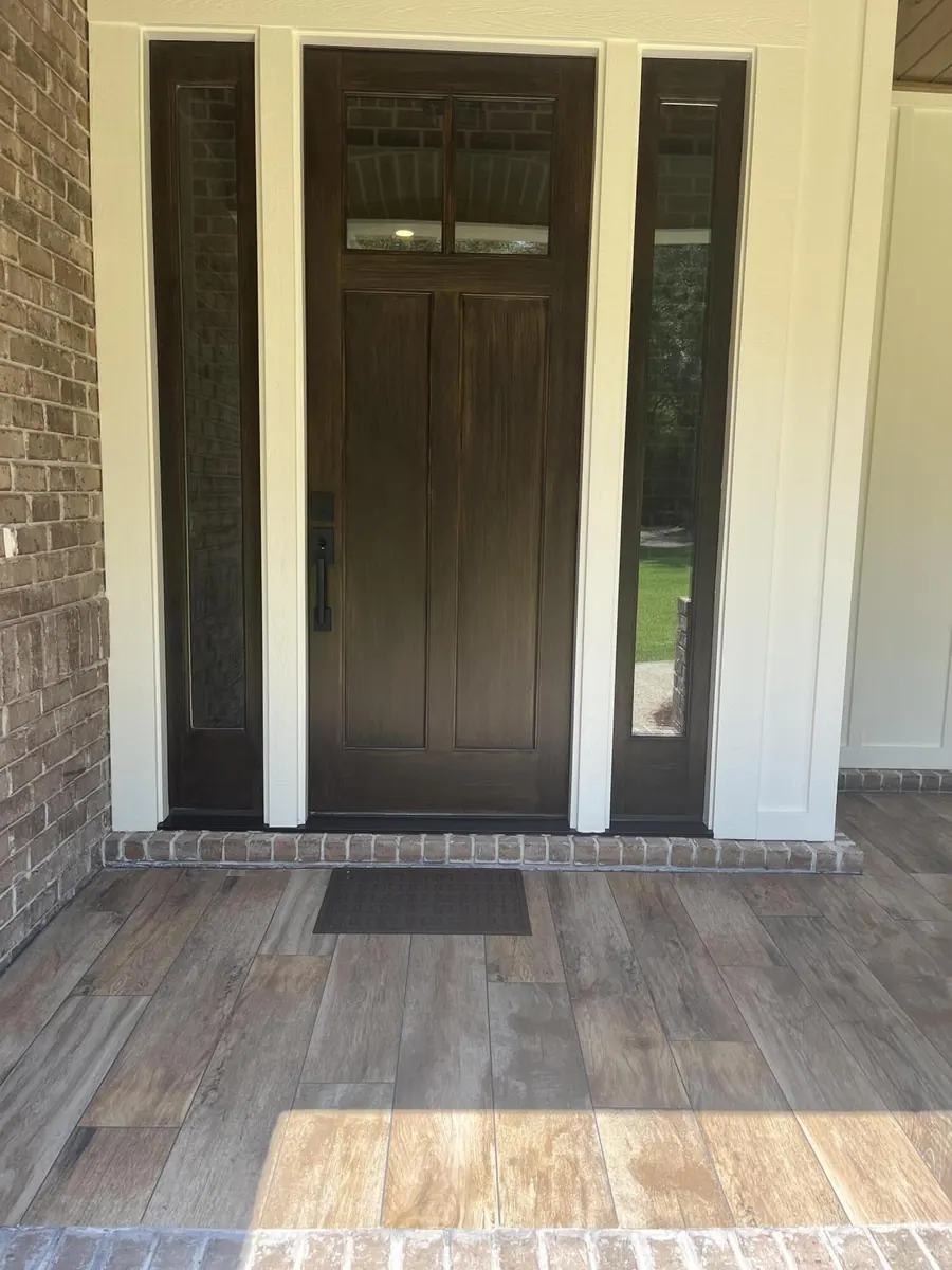 Dark-stained craftsman front door with glass sidelights on a brick front porch