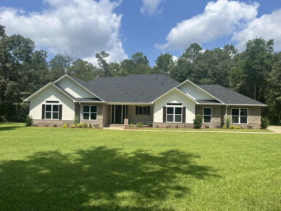 Front of the brick home with white gables and black-framed windows on a wide green lawn