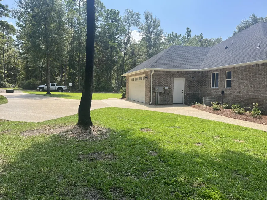 Side-entry garage and paved drive on the brick home, shaded by a tall pine