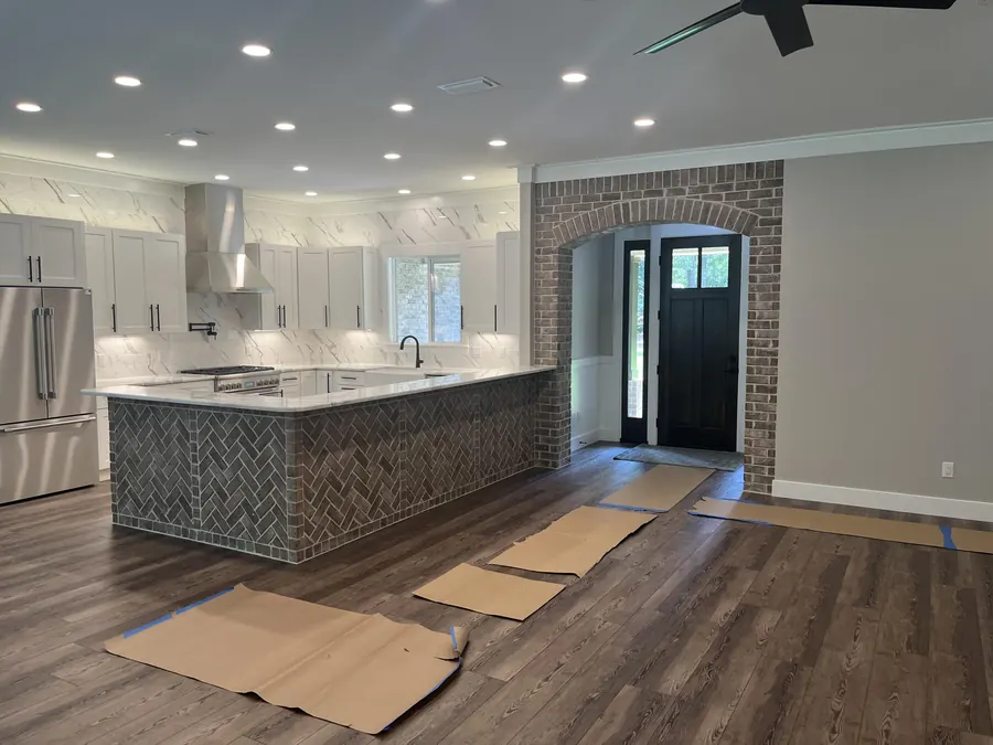 Open great room and kitchen with a brick-wrapped island, recessed lighting and wide-plank floors