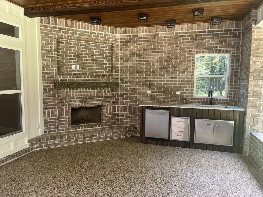 Screened porch with a brick fireplace, outdoor kitchen cabinets and a stained wood ceiling