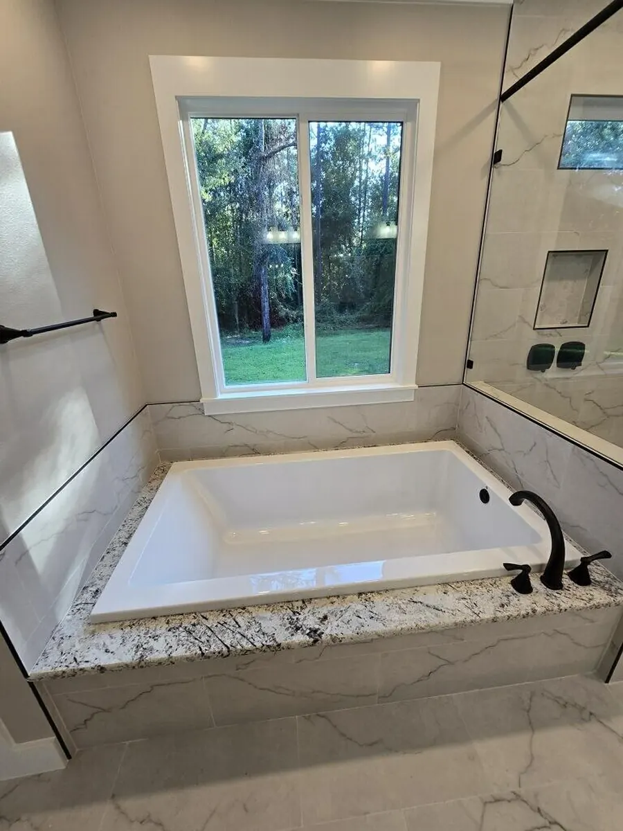 Large soaker tub set in granite under a window, with a glass walk-in shower beside it