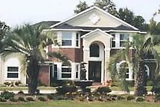 Two-story stucco and brick home with palm trees and an arched entry