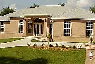 Tan brick home with an arched entry, a brick mailbox and a curving drive